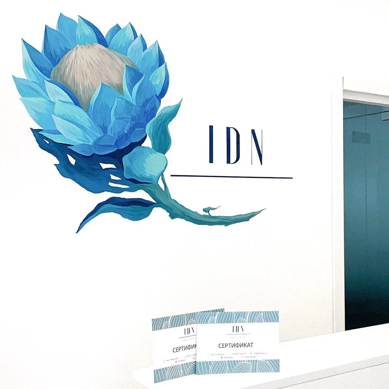 Брендинг IDN Skin & Hair Clinic — стіна рецепції з логотипом IDN та подарунковими сертифікатами.